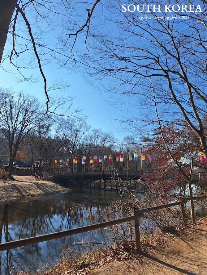A scenic view of a wooden bridge over a river in Gyeonggi-do, South Korea, decorated with traditional colorful lanterns under a clear blue sky.