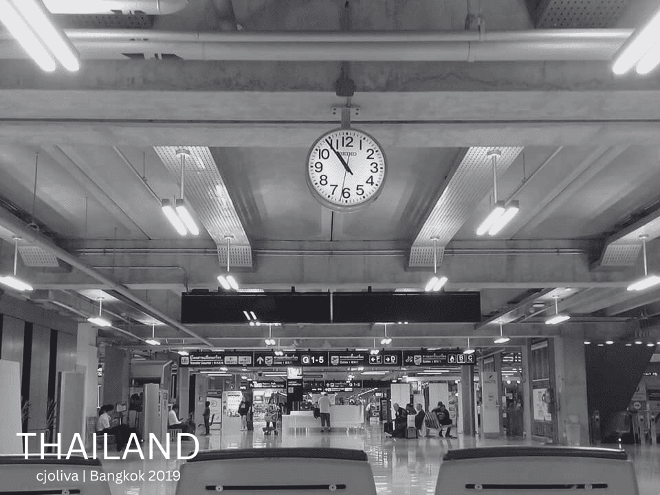 A black and white image of Suvarnabhumi Airport interior showing clock, seating area, and passengers in Bangkok