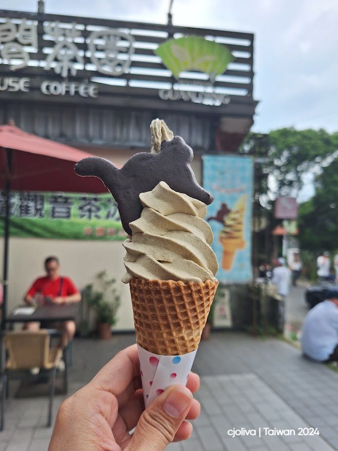 Soft-serve ice cream in a waffle cone topped with a squirrel-shaped cookie at the Guanziling coffee shop in Taiwan, with the storefront and people in the background.