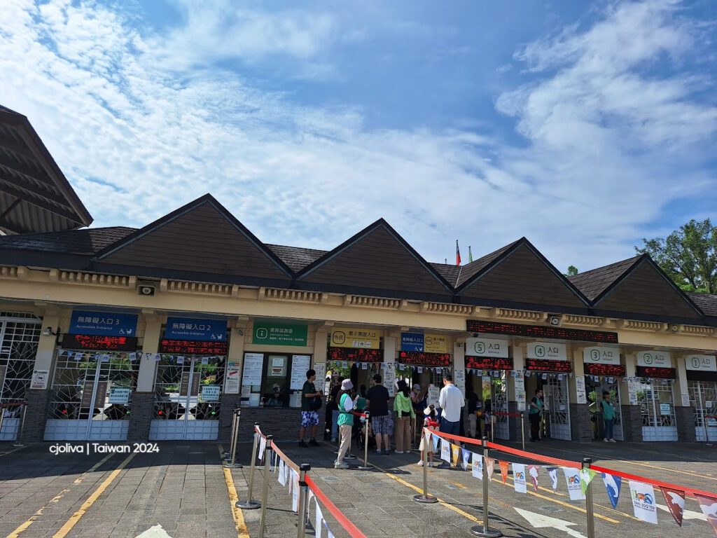 Entrance gates at Taipei Zoo in Taiwan with peaked roofs, numbered ticket booths, accessible entrances, electronic displays, and signage for Panda House.