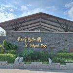 Entrance to Taipei Zoo in Taiwan with a stone wall, golden Chinese and English text, animal statues, and a slanted metal roof surrounded by greenery.