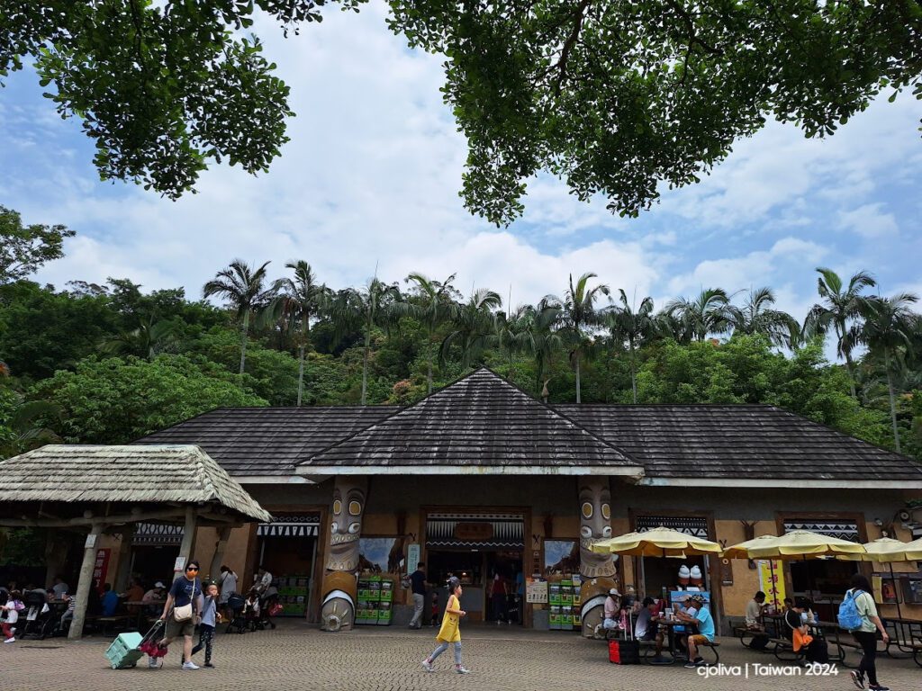 Ticket gates at Taipei Zoo in Taiwan with numbered entrances, accessible signs, colorful flags, and visitors queuing under a triangular roof.