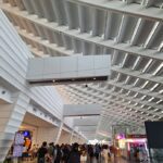 Modern airport terminal in Taiwan with geometric ceiling panels, skylights, travelers with suitcases, flight information display, and China Airlines counters.