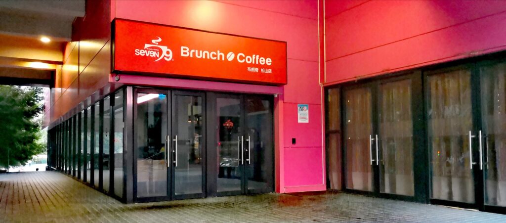 Exterior of seven9 Brunch Coffee in Taipei with a bright red sign, Chinese characters, pink walls, glass double doors, and a tiled walkway.