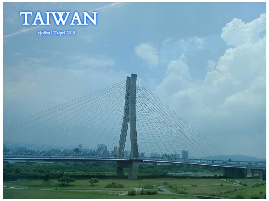 Cable‑stayed bridge in Taipei, Taiwan, with a central pylon, diagonal cables, a wide river, green fields, and urban buildings under a partly cloudy sky.