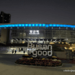 Night view of Busan Station in South Korea with illuminated "Busan is good" sign and blue lights on the station roof.