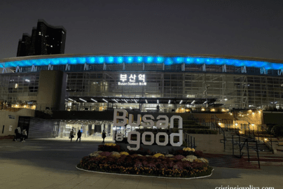 Night view of Busan Station in South Korea with illuminated "Busan is good" sign and blue lights on the station roof.