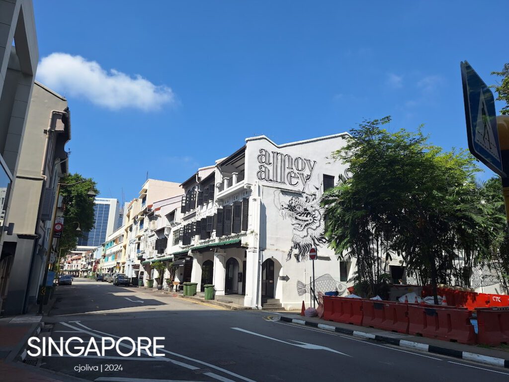 Colorful Singapore shophouses with a dragon mural on Amoy Alley, blending heritage architecture with modern high-rises in the background.