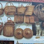 Mural in Singapore depicting woven baskets, straw hats, and two painted cats—one sleeping in a basket and one sitting upright—beneath a red-tiled roof.