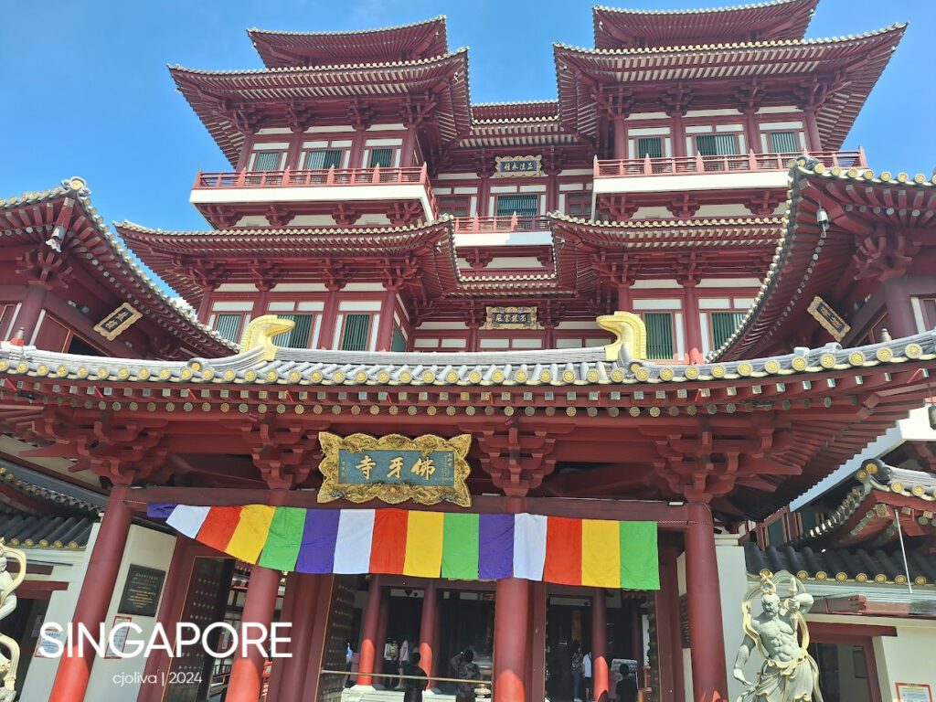 Ornate Buddha Tooth Relic Temple in Singapore’s Chinatown with red pillars, golden details, and prayer flags under a clear blue sky.