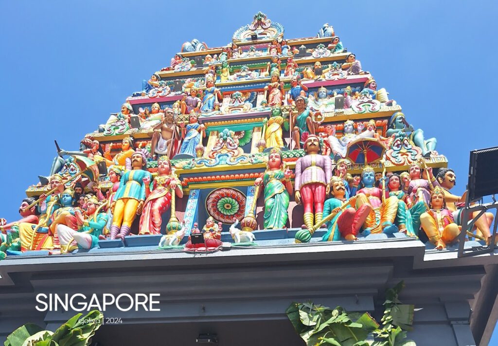 Ornate Hindu temple gopuram in Singapore with vividly painted deities, mythological figures, and colorful motifs against a clear blue sky.
