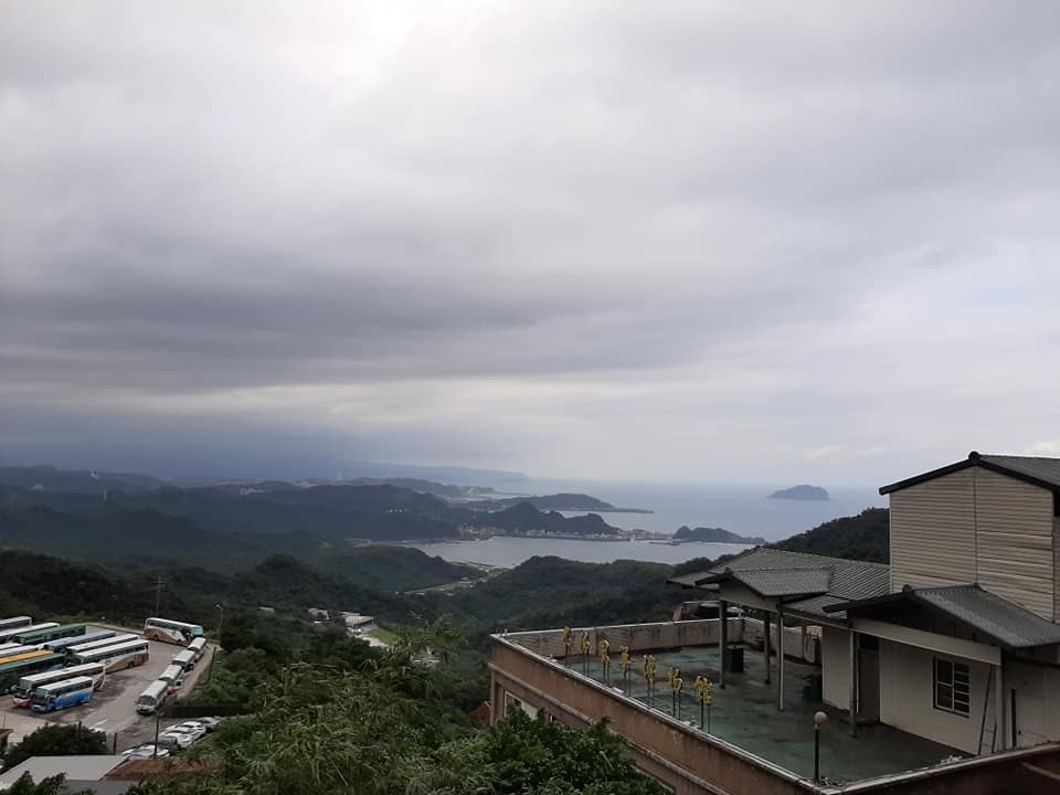 Elevated view from Jiufen Street in New Taipei, Taiwan, showing green hills, coastal town, ocean with islands, and cloudy sky, taken in 2019