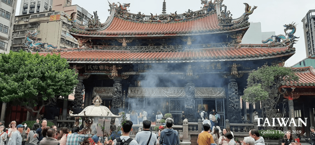 Longshan Temple with ornate roof carvings, incense smoke, and worshippers in Taipei, Taiwan.