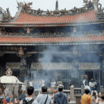 Longshan Temple with ornate roof carvings, incense smoke, and worshippers in Taipei, Taiwan.