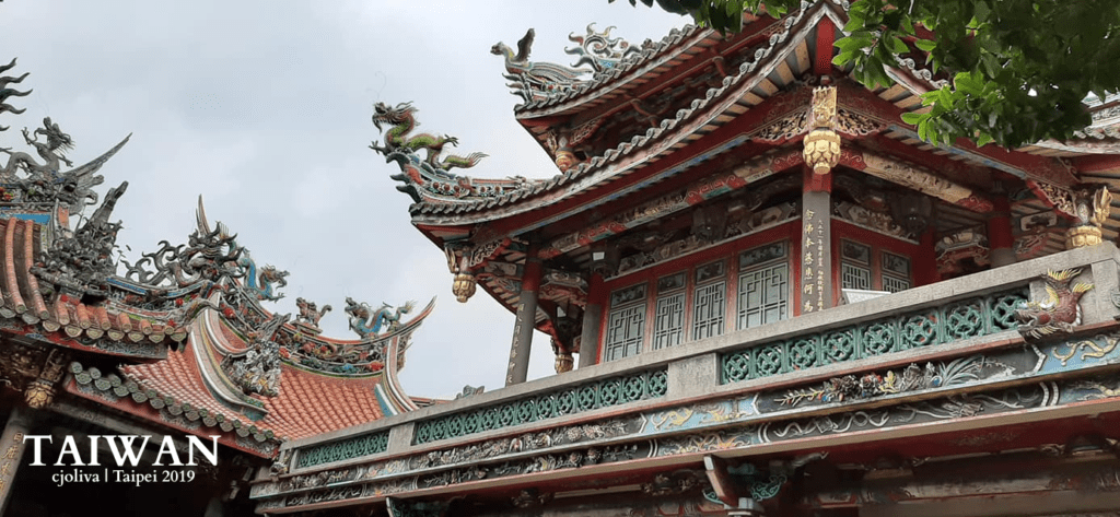 Longshan Temple with ornate roof carvings, dragon sculptures, and worshippers in Taipei, Taiwan.