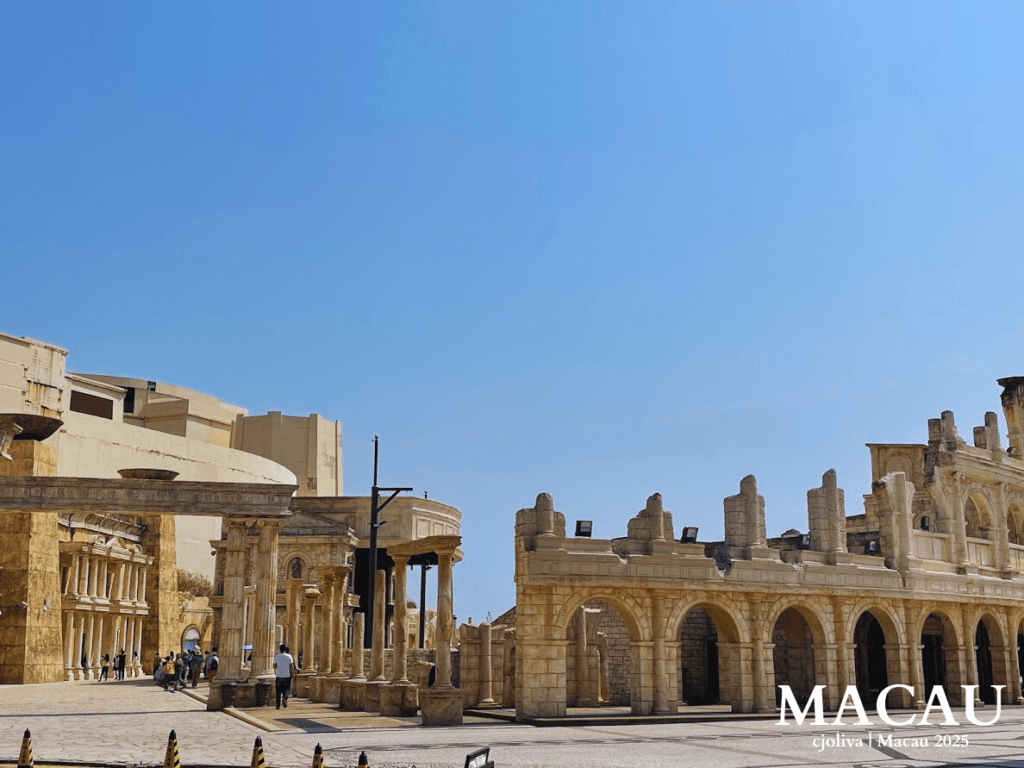 Classical Roman-style stone arches and columns at Macau Fisherman's Wharf under a clear blue sky.