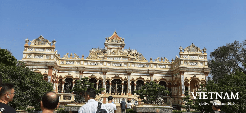 Intricately designed temple facade in the Mekong River Delta with visitors admiring the architecture on a sunny day.