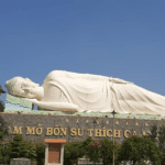 Reclining Buddha statue at a temple visited on the Mekong River Delta Tour, surrounded by lush greenery and clear blue sky.
