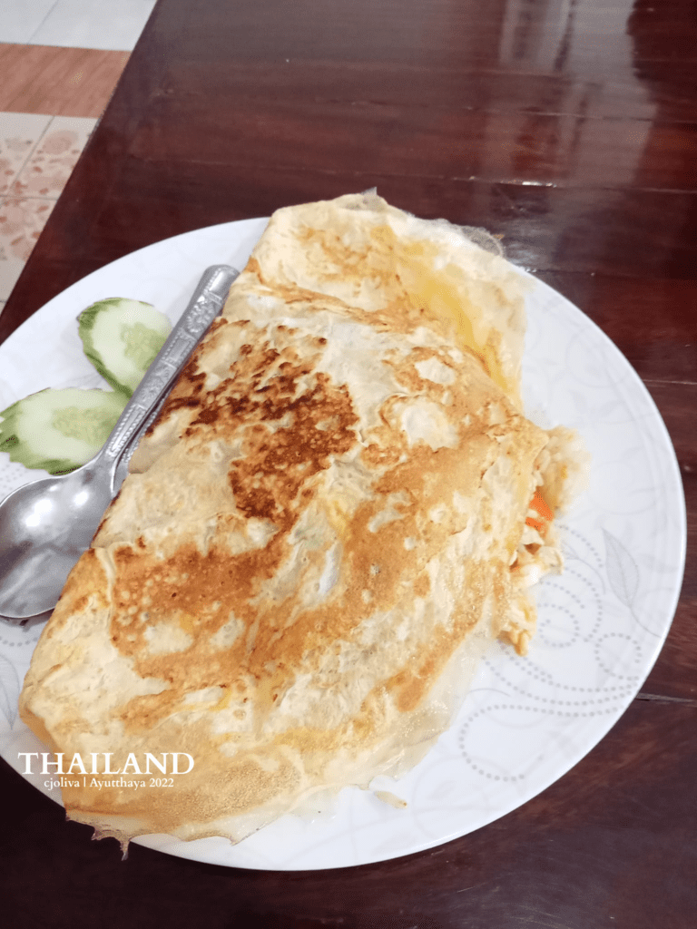 Traditional stuffed omelette served with cucumber slices on a floral plate in Ayutthaya, Thailand