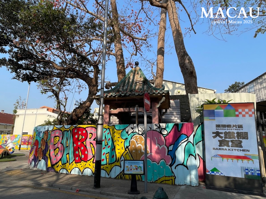 A colorful "BARRA" graffiti mural on a corrugated metal fence, with a traditional Chinese-style pavilion tucked behind large banyan trees and a modern "Barra Kitchen" sign in the foreground.