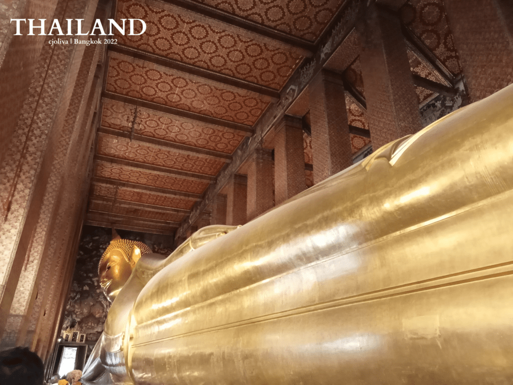 Golden Reclining Buddha statue at Wat Pho temple in Bangkok inside ornately decorated hall with patterned ceiling and tall columns
