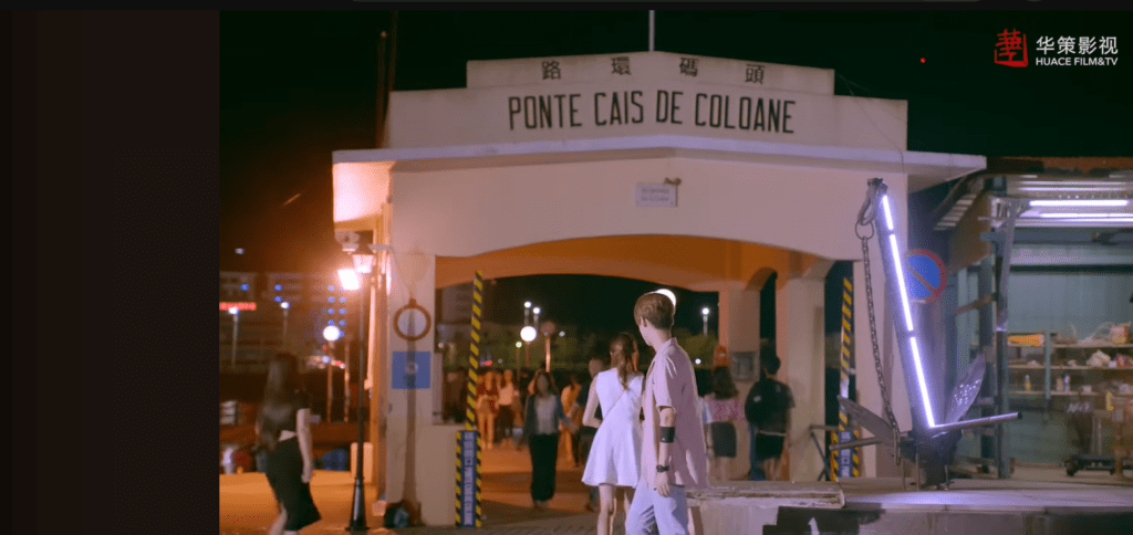Nighttime scene from the C-Drama Sweet Combat starring Lu Han and Guan Xiao Tong, filmed at Coloane Pier in Macau with illuminated signage and a nautical anchor display.