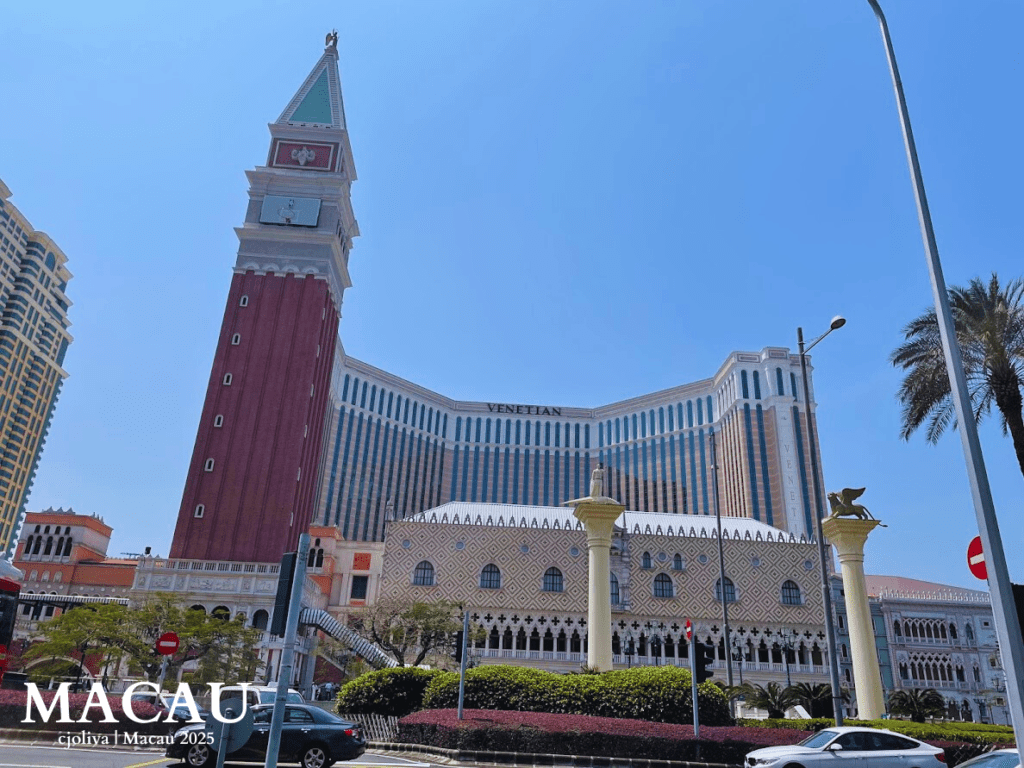 A wide view of The Venetian Macao resort featuring the replica St. Mark's Campanile bell tower and the Doge's Palace architecture against a clear blue sky.
