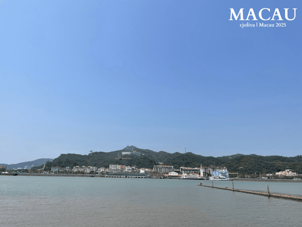 A view across the narrow Shisanmen Waterway from the Coloane Village waterfront, showing the modern high-rise buildings and hills of Hengqin Island, Zhuhai, in mainland China.