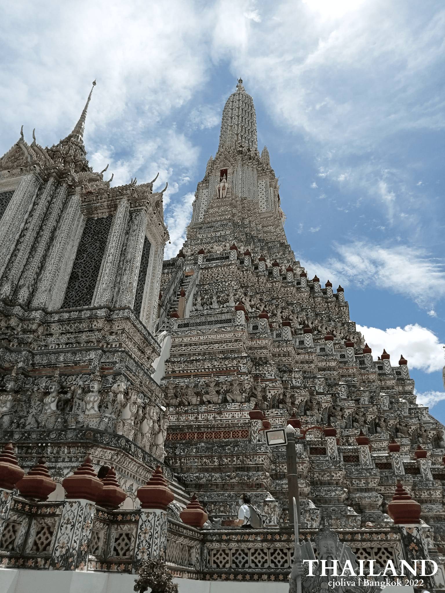 Ornate Wat Arun temple in Bangkok with towering prang decorated in porcelain under a partly cloudy sky