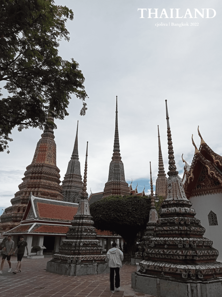 Ornate stupas at Wat Pho temple in Bangkok decorated with colorful tiles, surrounded by traditional Thai architecture and visitors under an overcast sky