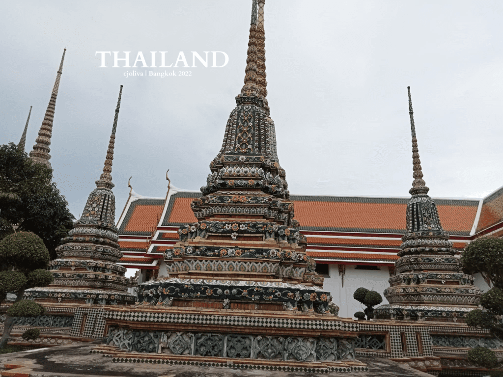 Colorful stupas at Wat Pho temple in Bangkok decorated with ceramic tiles and floral motifs beside a traditional Thai building