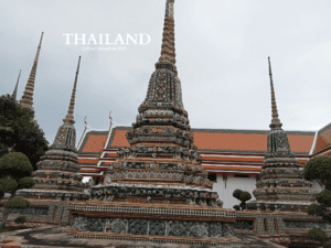 Colorful stupas at Wat Pho temple in Bangkok decorated with ceramic tiles and floral motifs beside a traditional Thai building