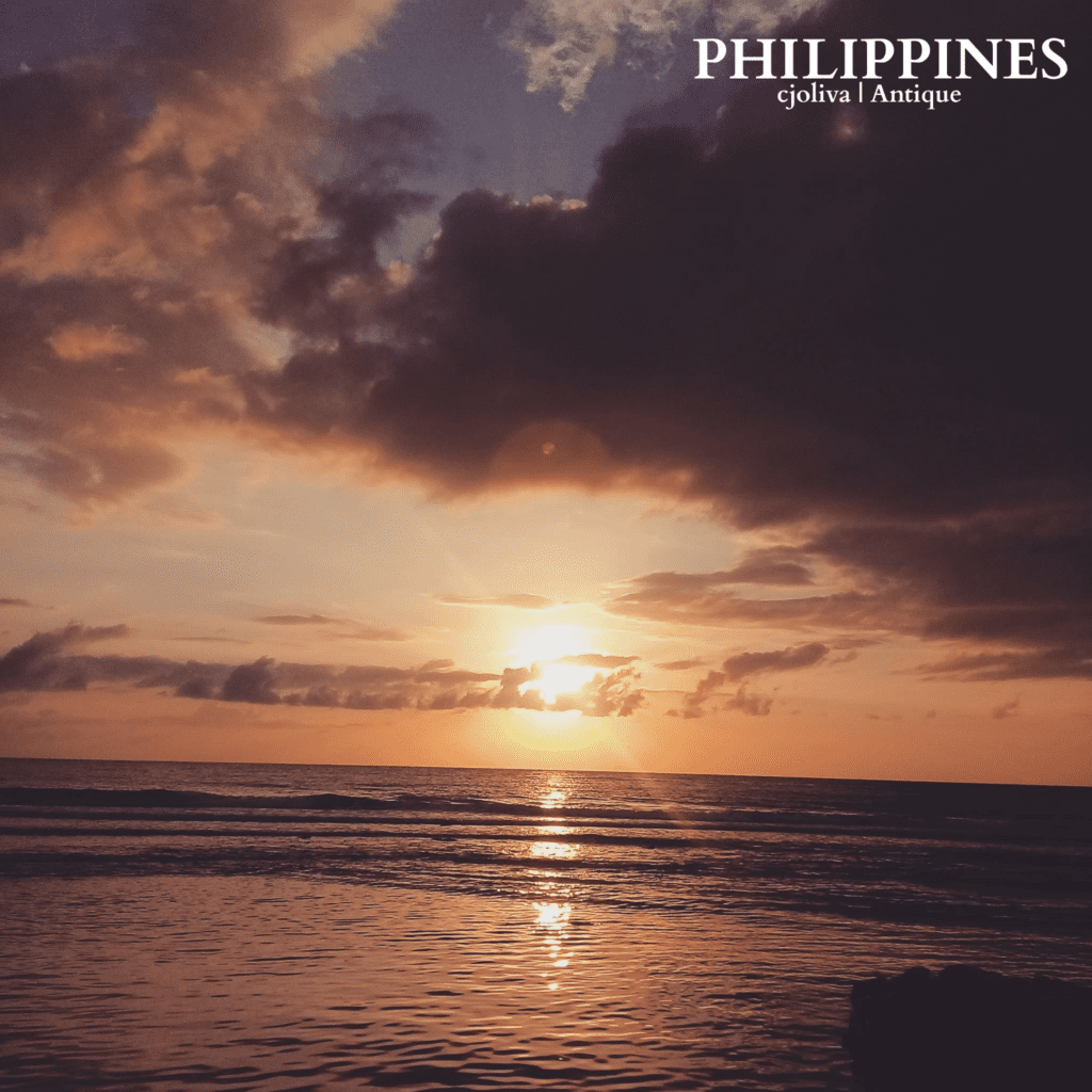 Scenic sunset view over the ocean in Antique, Philippines, with golden and orange sky, calm water reflections, gentle waves, and dramatic clouds, taken in 2018