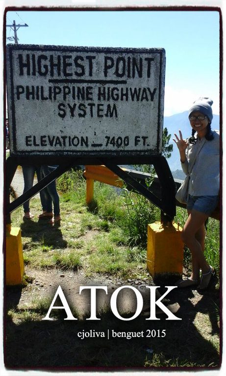 Tourist posing next to a sign marking the highest point of the Philippine Highway System at 7,400 feet in Atok, Benguet, in 2015.