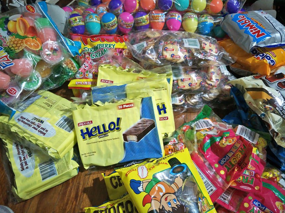 Various colorful snack and candy packs, including Hello vanilla wafers, Chocobons, Happy Egg chocolate eggs, and other treats, are arranged on a table.