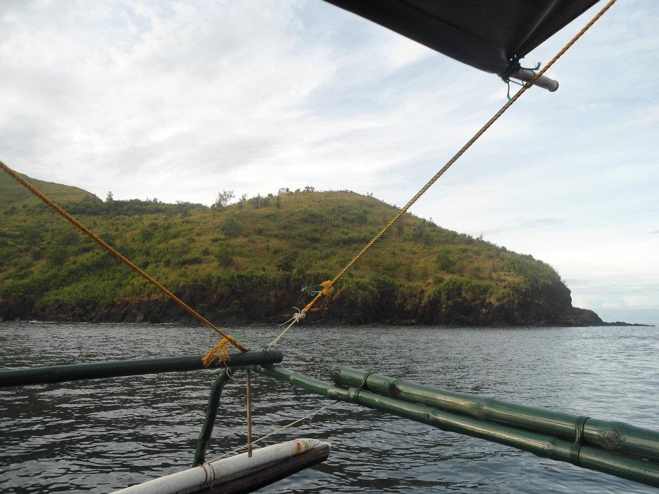 Scenic tropical island with rocky shoreline seen from a traditional Philippine banca with bamboo outriggers