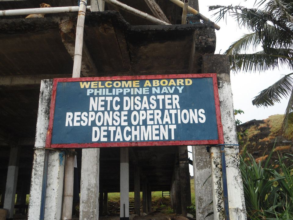 Weathered signboard reading “Philippine Navy NETC Disaster Response Operations Detachment” in front of a deteriorating building with tropical vegetation