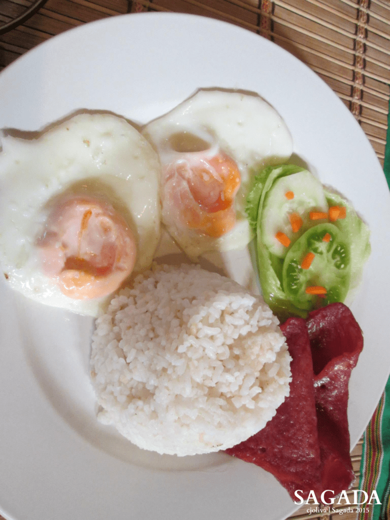 Traditional Filipino breakfast in Sagada with fried eggs, white rice, cured meat slices, and fresh vegetables on a bamboo mat.