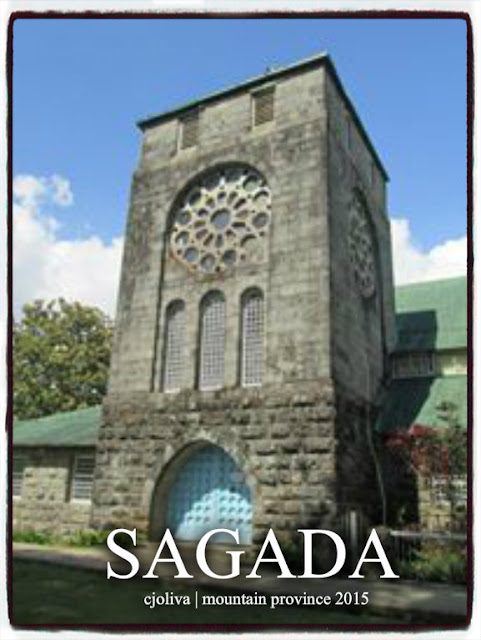 Historic stone church in Sagada, Mountain Province, with a tall tower, circular stained-glass window, arched doorway, and green roof under a partly cloudy sky.