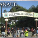 Tourists gathered under the "Welcome to Banaue" archway sign at the entrance to Banaue, surrounded by greenery and vehicles in the background.