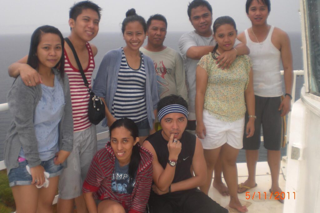 Nine people posing together on a dock or boat with the ocean in the background, dressed casually during an overcast seaside trip, dated May 11, 2011