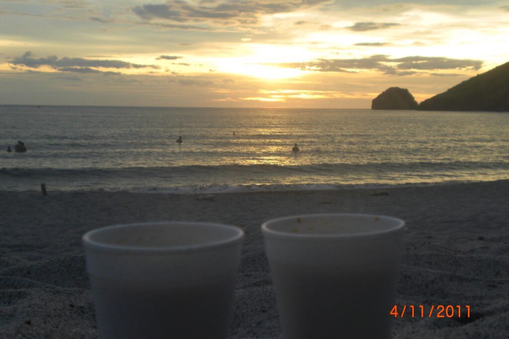 Golden sunset over calm ocean waters with people swimming and disposable cups on sandy beach, dated April 11, 2011