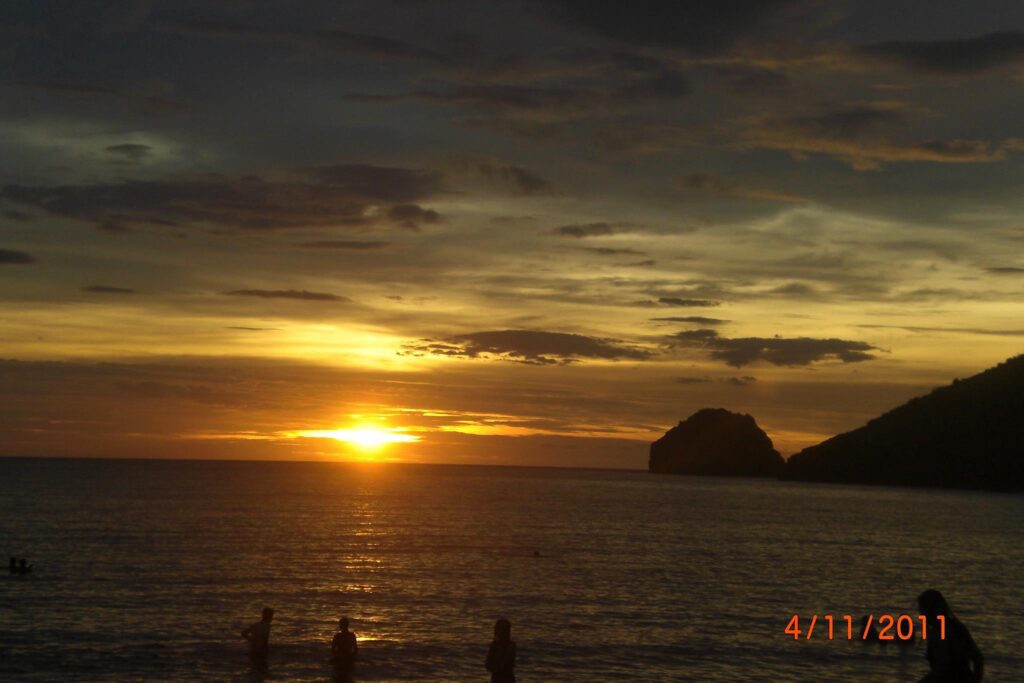Scenic sunset over the ocean with silhouettes of people on the shore and golden reflection on the water, dated April 11, 2011