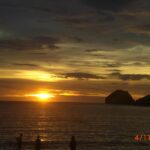 Scenic sunset over the ocean with silhouettes of people on the shore and golden reflection on the water, dated April 11, 2011