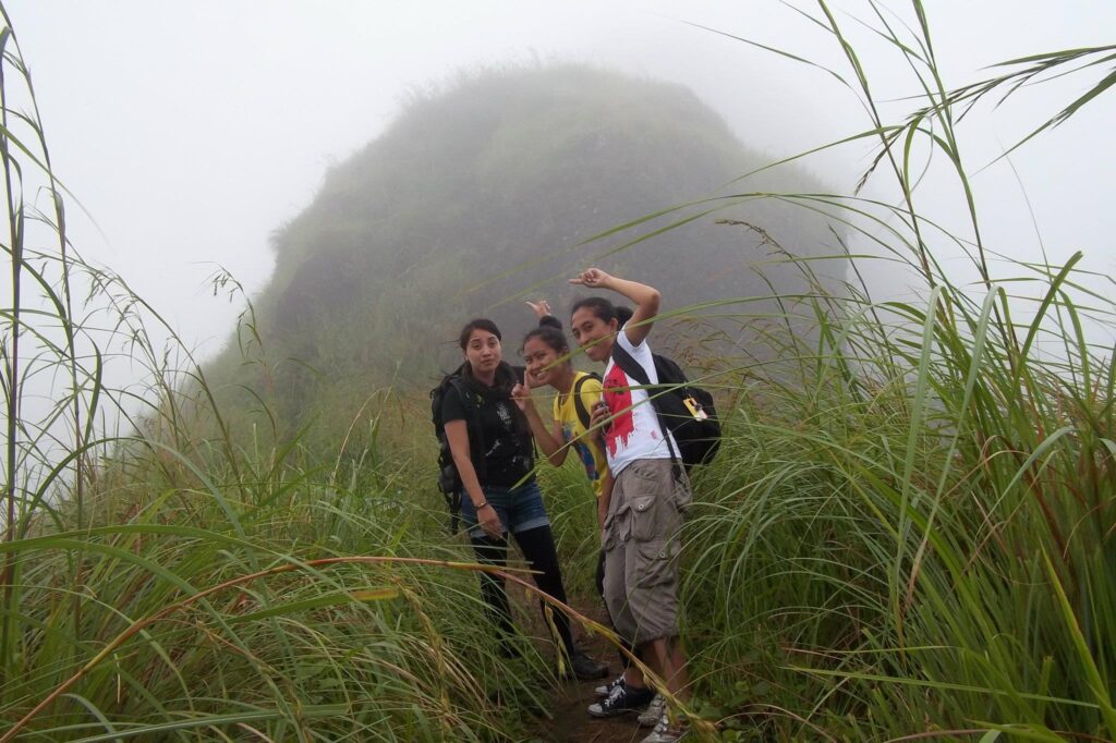 Three friends posing on a misty hiking trail of Mt. Batulao surrounded by tall green grass