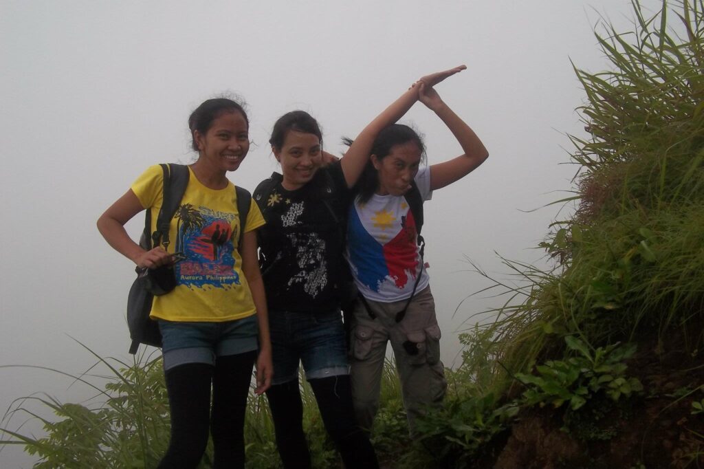 Three friends posing playfully on a foggy mountain trail at Mt. Batulao, wearing casual hiking clothes and backpacks