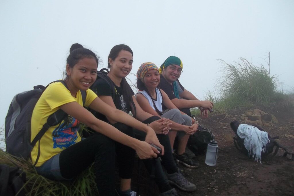 Four friends sitting and resting on a foggy summit of Mt. Batulao with hiking gear and backpacks