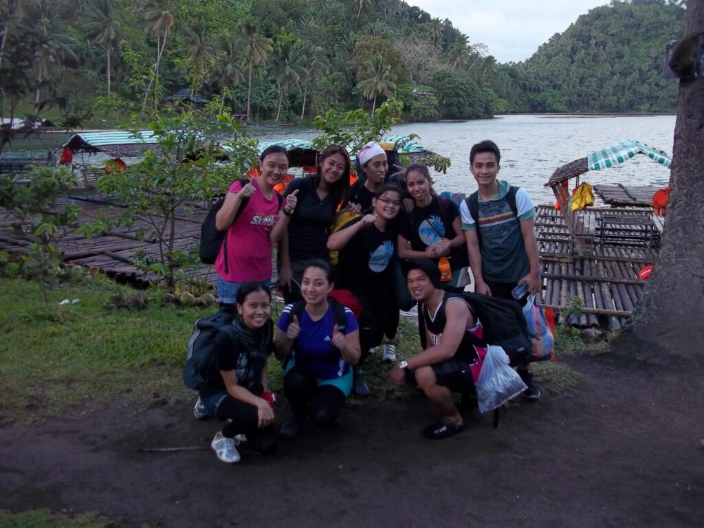 Group of smiling friends posing for a photo near bamboo rafts on the shore of Lake Pandin with lush hills in the background, Laguna 2013.