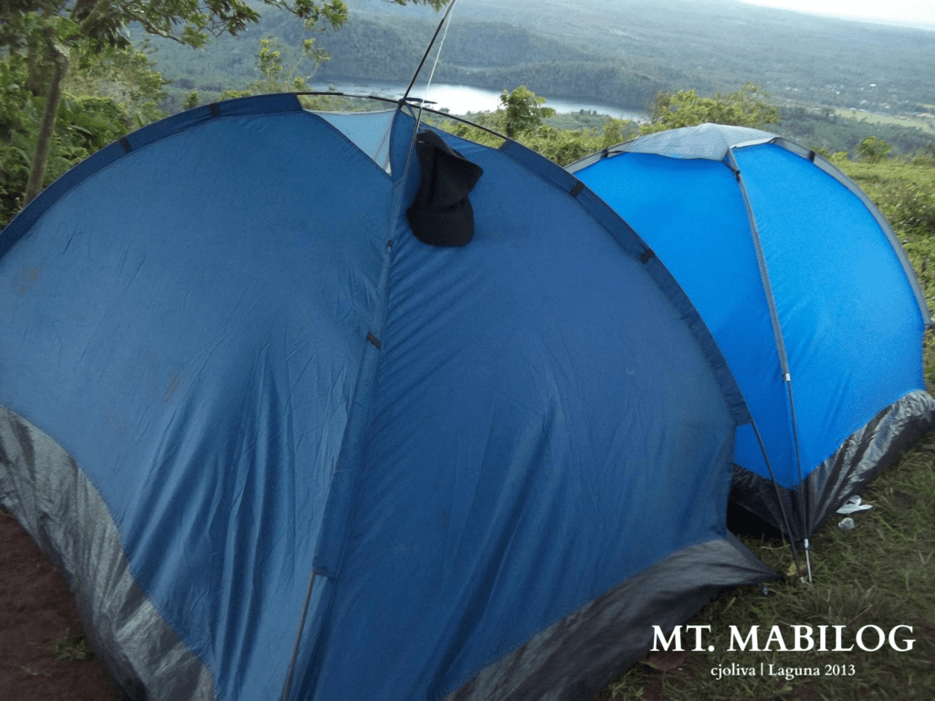 Two blue camping tents set up on Mt. Mabilog in Laguna with a scenic view of a lake and forested hills in the background, taken in 2013.