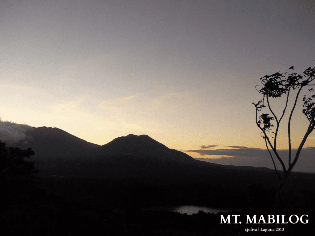 Scenic view of Mt. Mabilog in Laguna, Philippines, during sunrise, with silhouetted peaks, gradient sky, and trees by a small body of water, taken in 2013